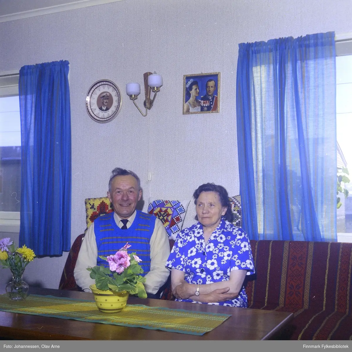 Foto av ukjent mann og kvinne i stue

Kongeparet henger på veggen 

Foto trolig tatt på 1960-tallet