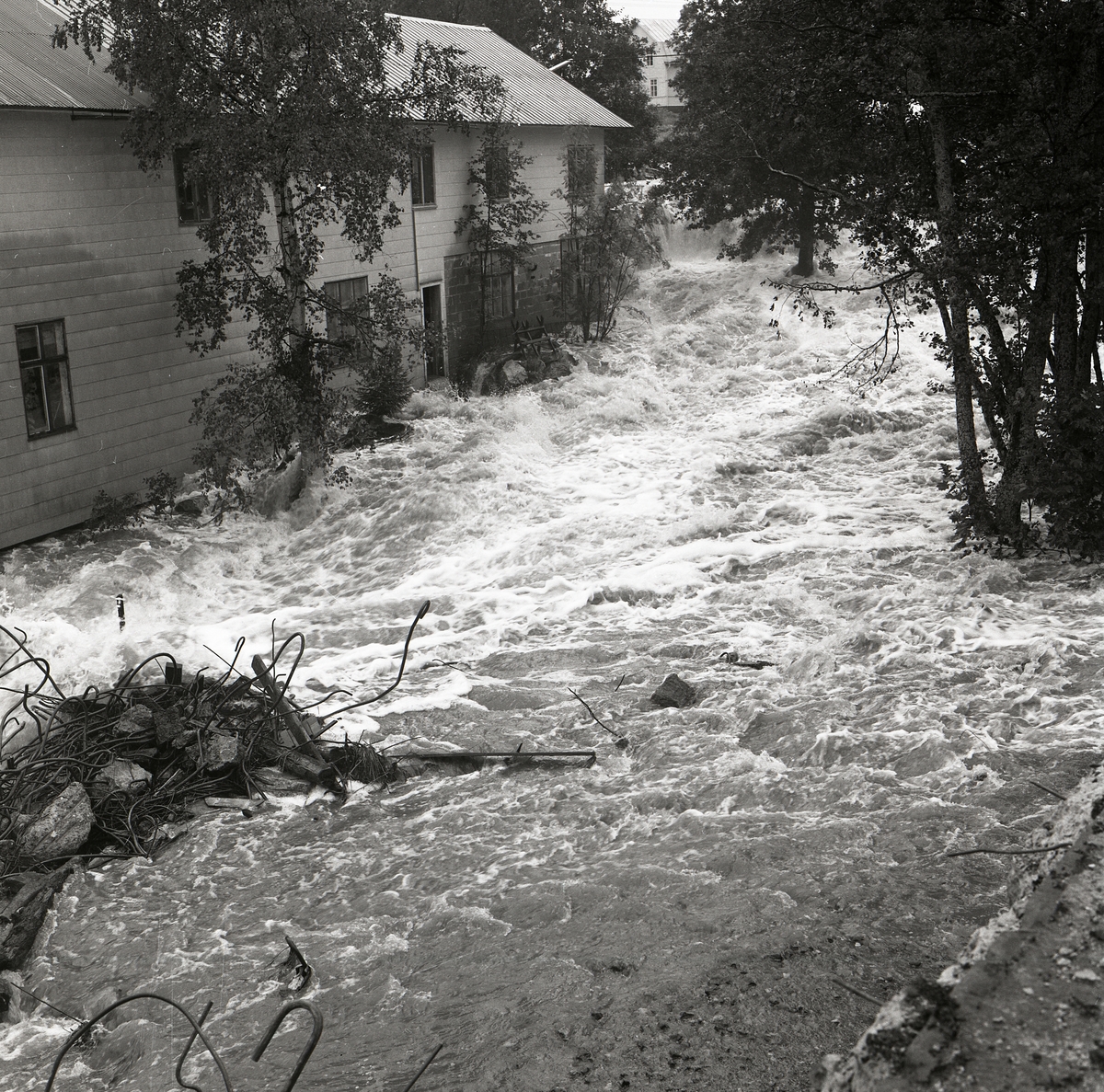 Vid en översvämning i Trönö forsar vatten fram förbi ett hus medan sten och bråte flyter med i vattenkraften, 1985.