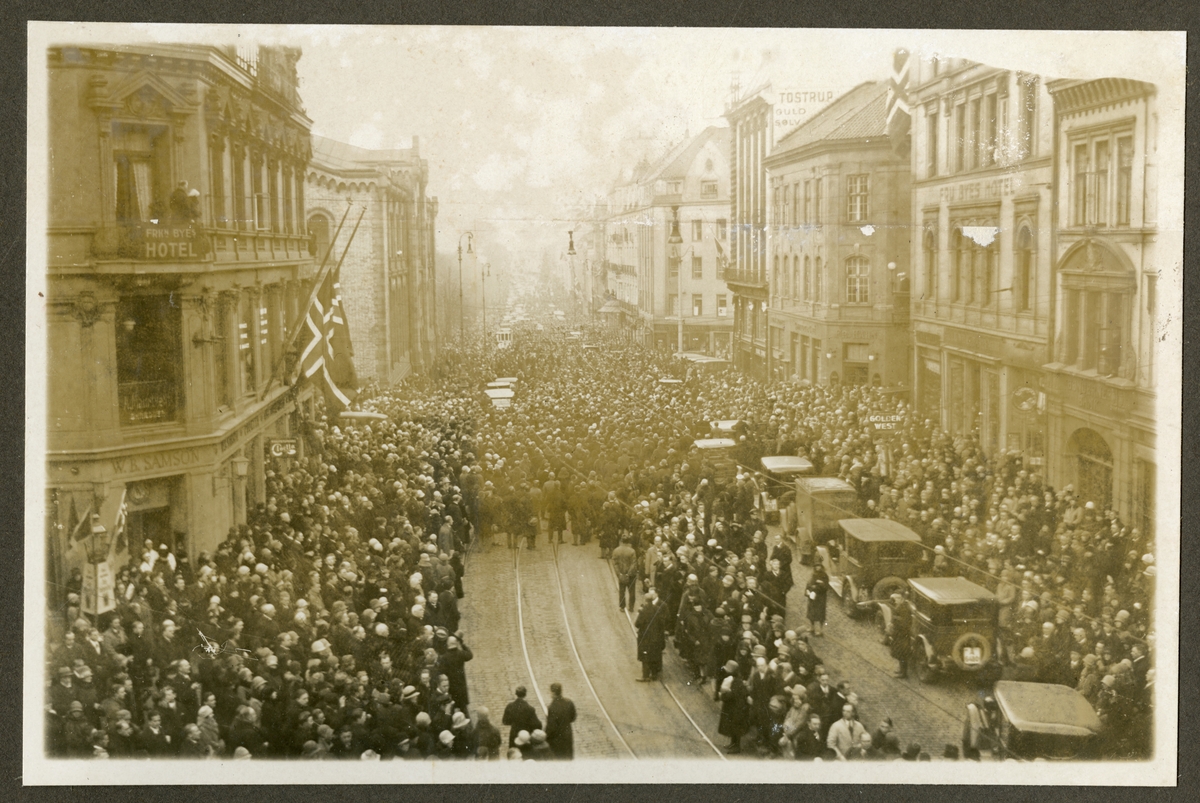 Gatebilde med flagging på halv stang. Tilskuere i gaten og foran Stortinget - Minnedagen for Roald Amundsen - 14. desember 1928. Fra stilheten i Oslo.
