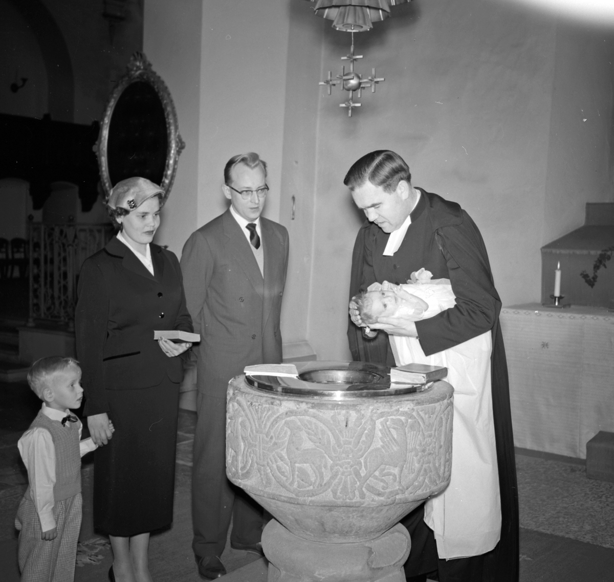 Familjen Mattson vid dopfuntet, prästen utför dopet
