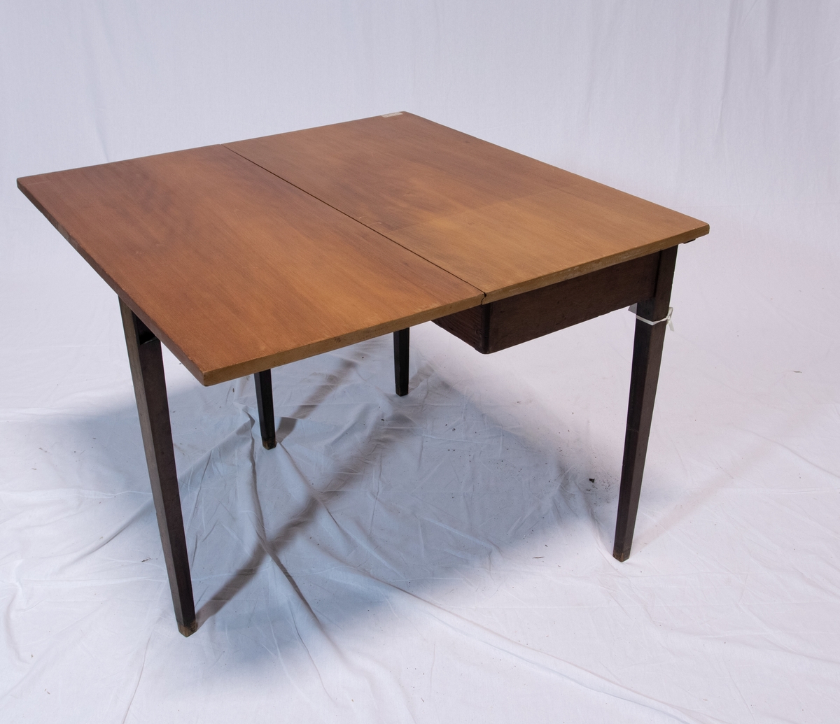Todelt spisebord bestående av to nesten like rektangulære brune bord med en hengslet rektangulær vinge hver. Det ene bordet har skuffe.