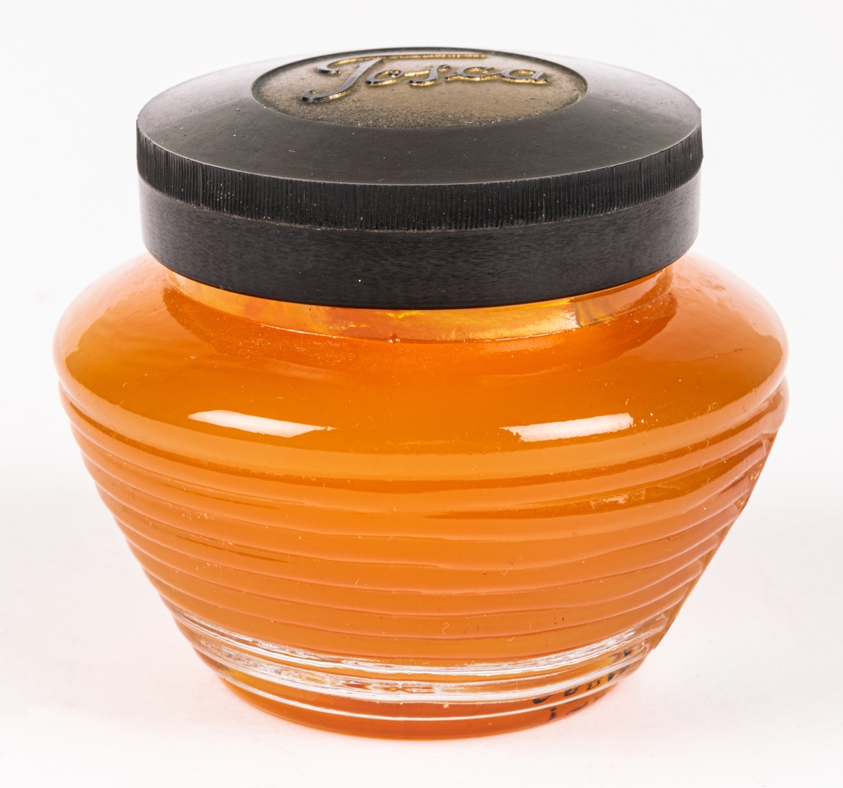 Glasburk med hårpomada (orginalförpackning). Genomskinligt glas med orangefärgad pomada. Svart lock med texten "TOSLA". På sidan en pappersetikett "4711 Tosca Brilliantine.