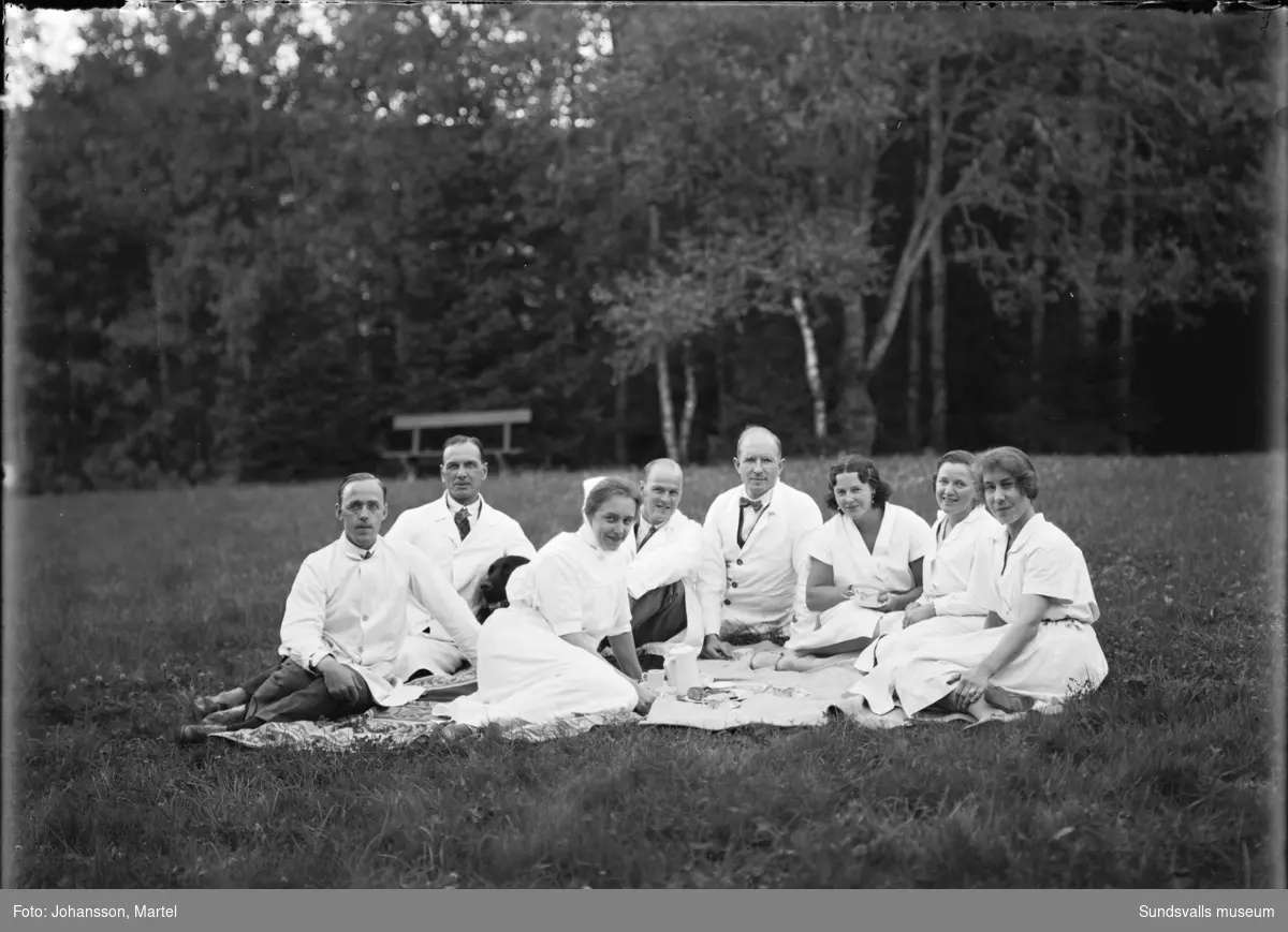 Gruppfoto med vårdpersonal sittande i gräset. I mitten fotografen själv, Martel Johansson.