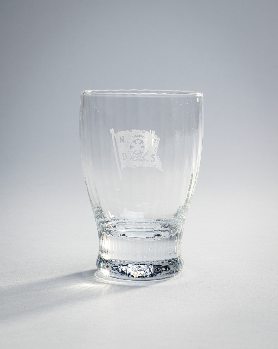 23 identiske vannglass fra NFDS (Nordenfjeldske Dampskibsselskap). De er tønneformet med tykk bunn/fot.  Det er loddrette riller i glasset som går fra bunnen og opp til åpningen. På glassene er logoen til NFDS slipt inn.