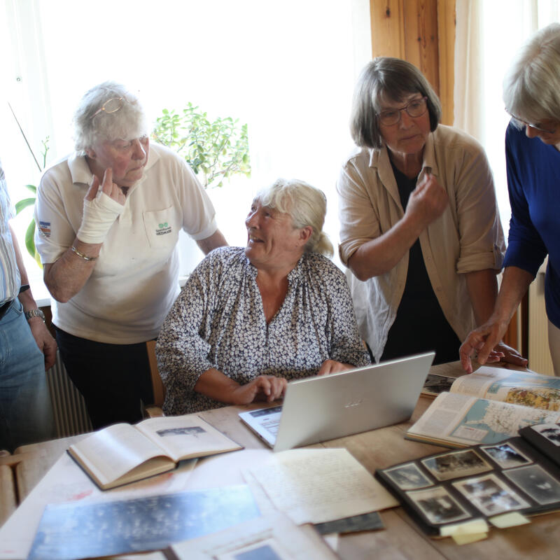 Venneforeningen tilbyr slektshjelp, frivillige rundt pc med arkiv materiale på bordet