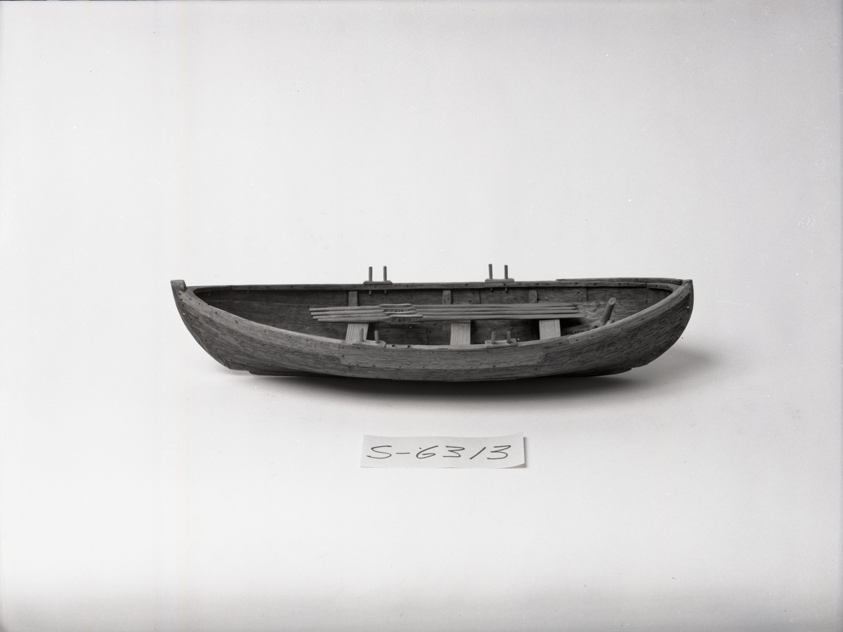 Båtmodell, rekonstruerad kopia av Kalmarfynd III, fullt utrustad. Bred kölplanka med stråkköl (ribba under) samt 4 bord på var sida, 3 spant, 4 årlägen för två roddare, 3 tofter, 4 åror.