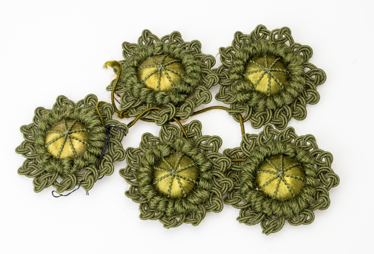 5 identiske rosetter brukt til møbler (møbelpossement). I midten er det en possementform av tre trukket med grønn silketråd og dekorert med tynn grønn silkesnor. Rosettene er laget av grønn ulltråd og grønn silketråd.