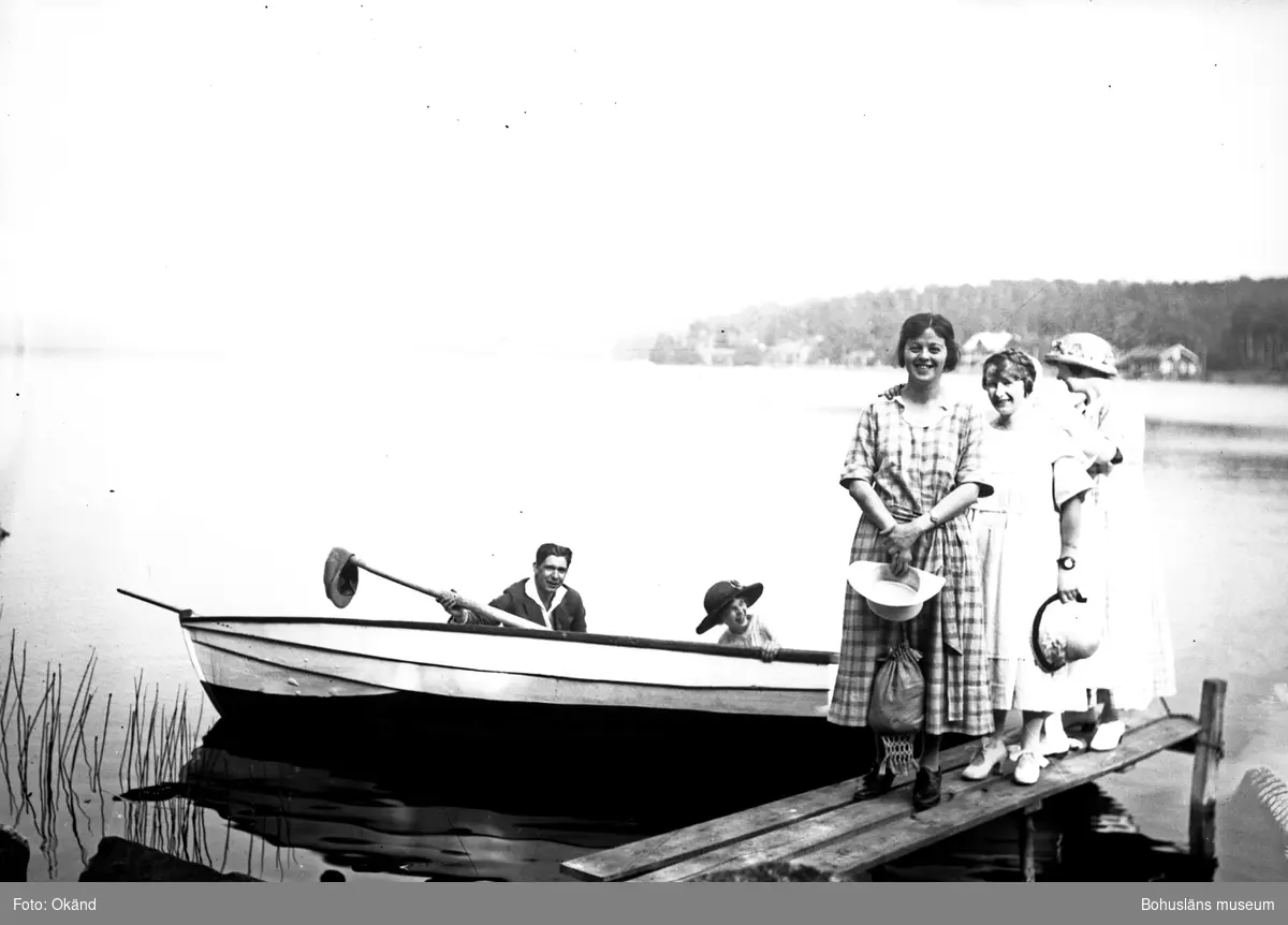 Två personer i en båt vid en brygga med tre personer på bryggan.