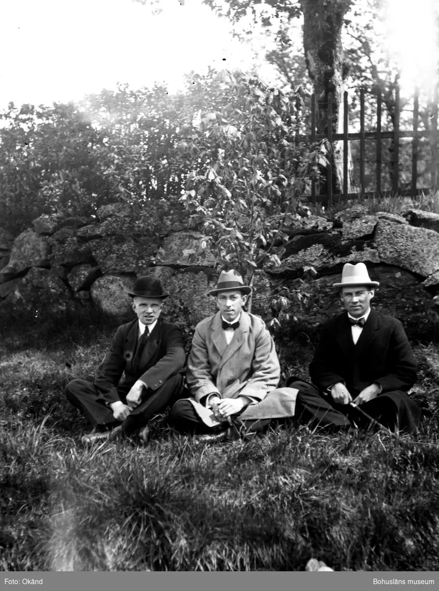 Tre personer sittandes i gräset framför en stenmur.