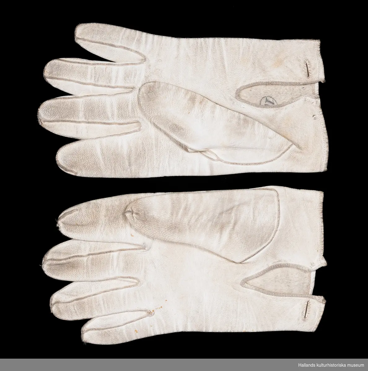 Två par bröllopshandskar av vitgarvat lammskinn. a-b) Herrhandskar. Längd 21 cm. c-d) Damhandskar. Längd 19 cm.