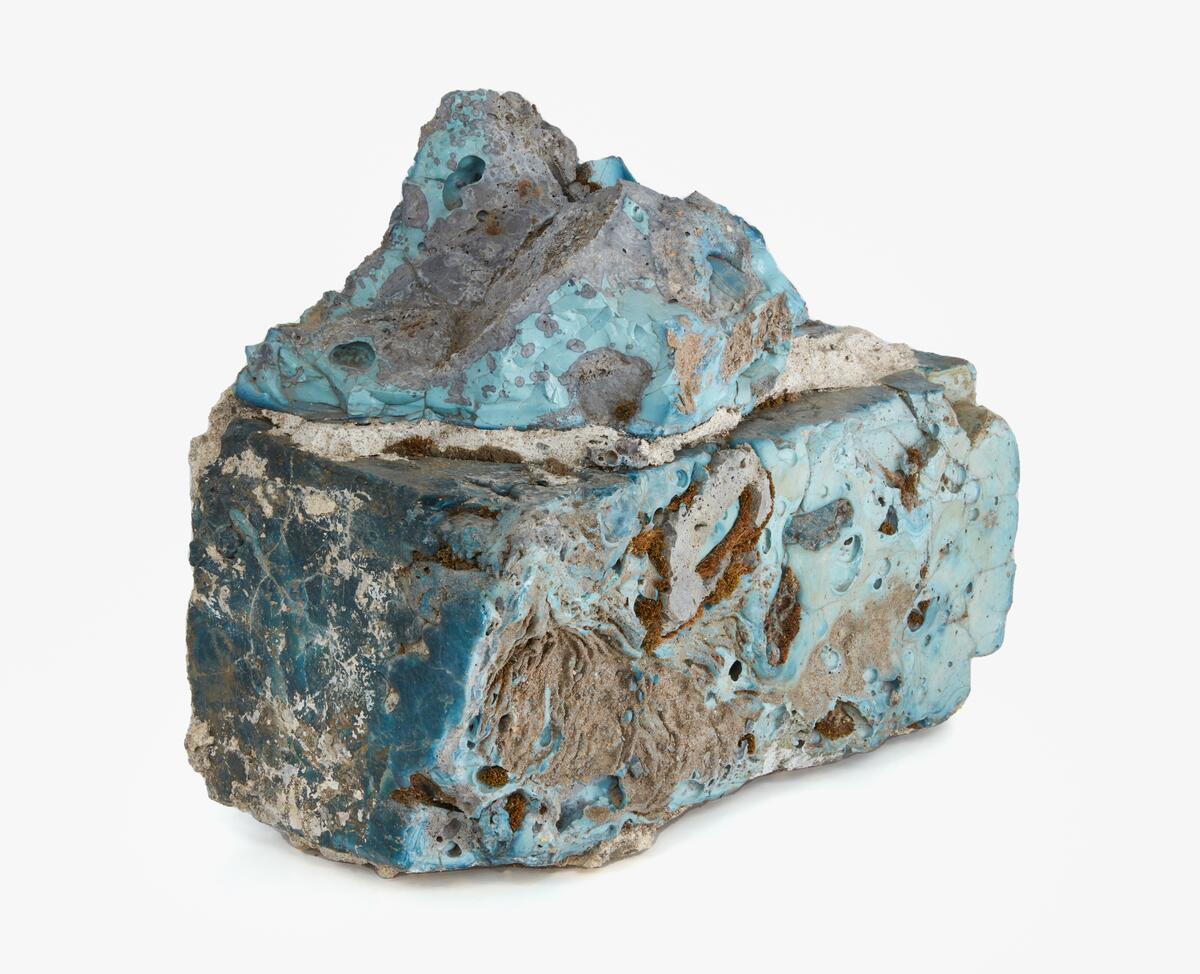 Byggsten av gjuten masugnsslagg. Troligen från järnbergslagen i södra Dalarna. Oregelbunden rektangulär form med utstickande delar som vittnar om att blocket en gång ingått i ett murverk. De höga temperaturerna vid järnframställningen har fått slaggens yttre skickt att omvandlas till glas. Kulörerna i detta skickt varierar kraftigt och beror på de mineraler som förekommer i malmen. Detta block är främst ljust- till mörkblått, vilket tyder på halter av kobolt och krom.