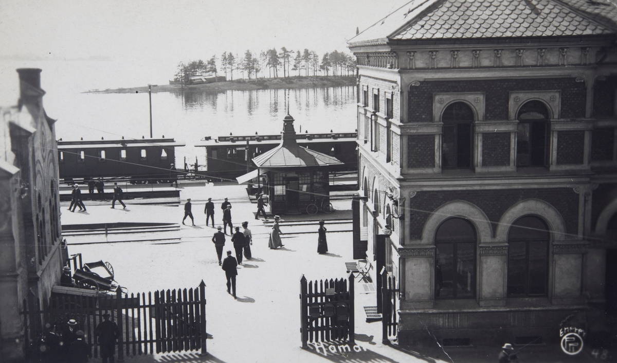 Postkort, Hamar Jernbanestasjon, perrong med Narvesenkiosk, togvogner, stakitt med port, reisende,