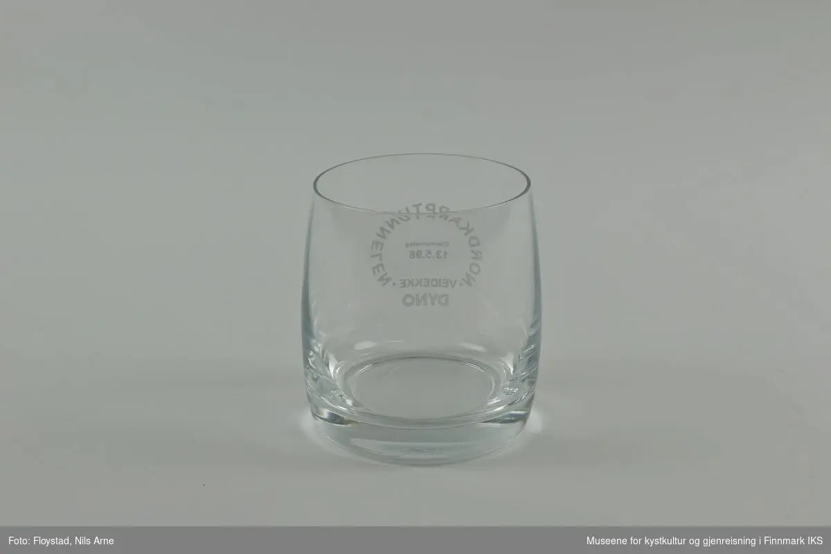 Et rundt brennevinsglass, eller cocktailglass uten stett og trykt tekst på siden av glasset. 

Glasset har en tykk bunn med tynne sider. Øverst står  "NORDKAPPTUNNELEN"  og nederst står "VEIDEKKE". Ordene danner en sirkel og "Gjennomslag 13.5.1998" er trykt inne i sirkelen. Helt nederst står "DYNO".   