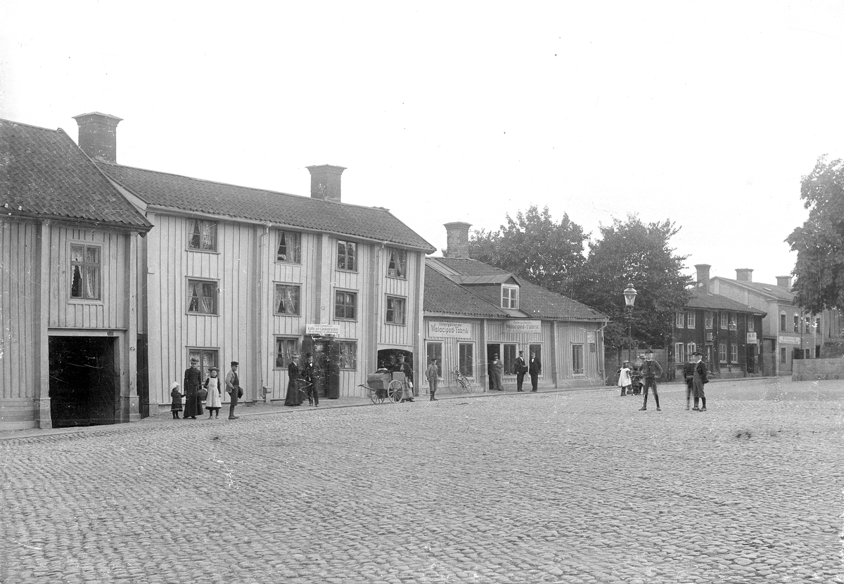 Vy över Järntorget i Linköping mot gårdarna på adresserna Storgatan 62-70. Trevåningsbyggnaden i blickfånget var i början av 1800-talet i familjen Pihls ägo, vilket namngivit gränden Pilens backe som mynnar ut genom valvet. Envåningsbyggnaden intill är den gamla Skolmästaregården, det vill säga rektorsbostad, och uppförd i slutet av 1600-talet. År 1897 blev mekanikern Karl August Pettersson ägare till gården och denne inredde där en av stadens första cykelverkstäder. Båda gårdarna är flyttade till friluftsmuseet Gamla Linköping.