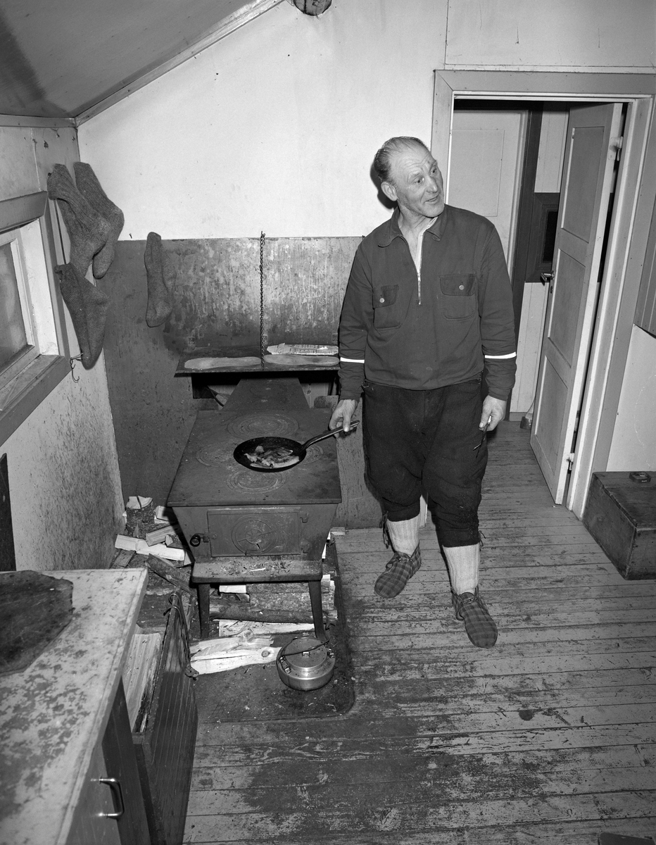 Skogsarbeider lager middag i koia. Johan Rasch steker flesk og poteter i Smaltjernkoia i Svartholtet, Elverum, Hedmark i januar 1975.