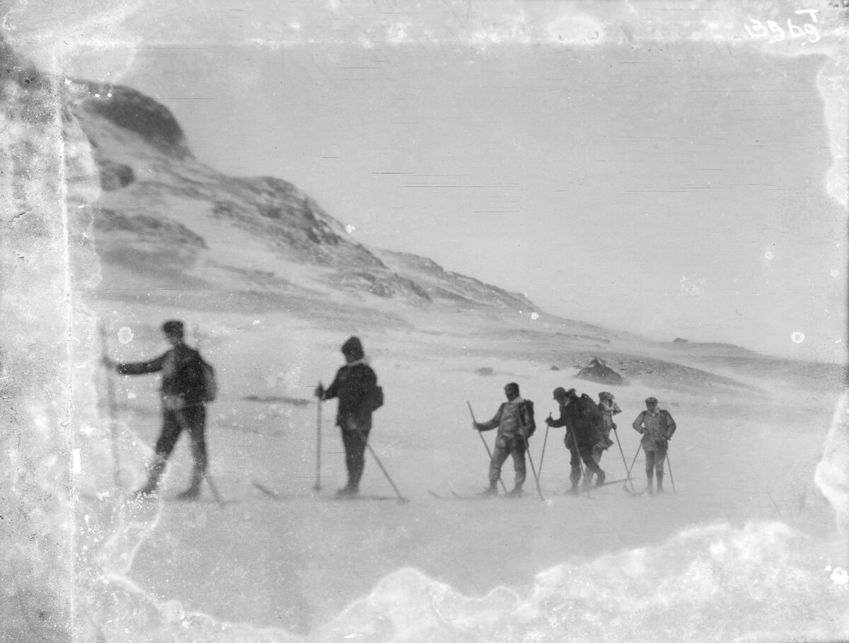 Seks menn på ski i et snødekket fjellandskap.