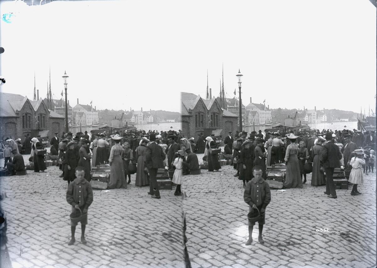 Stereofotografi. En folkemengde er samlet på Stavanger torg. I forgrunnen står en gutt vendt mot kameraet.