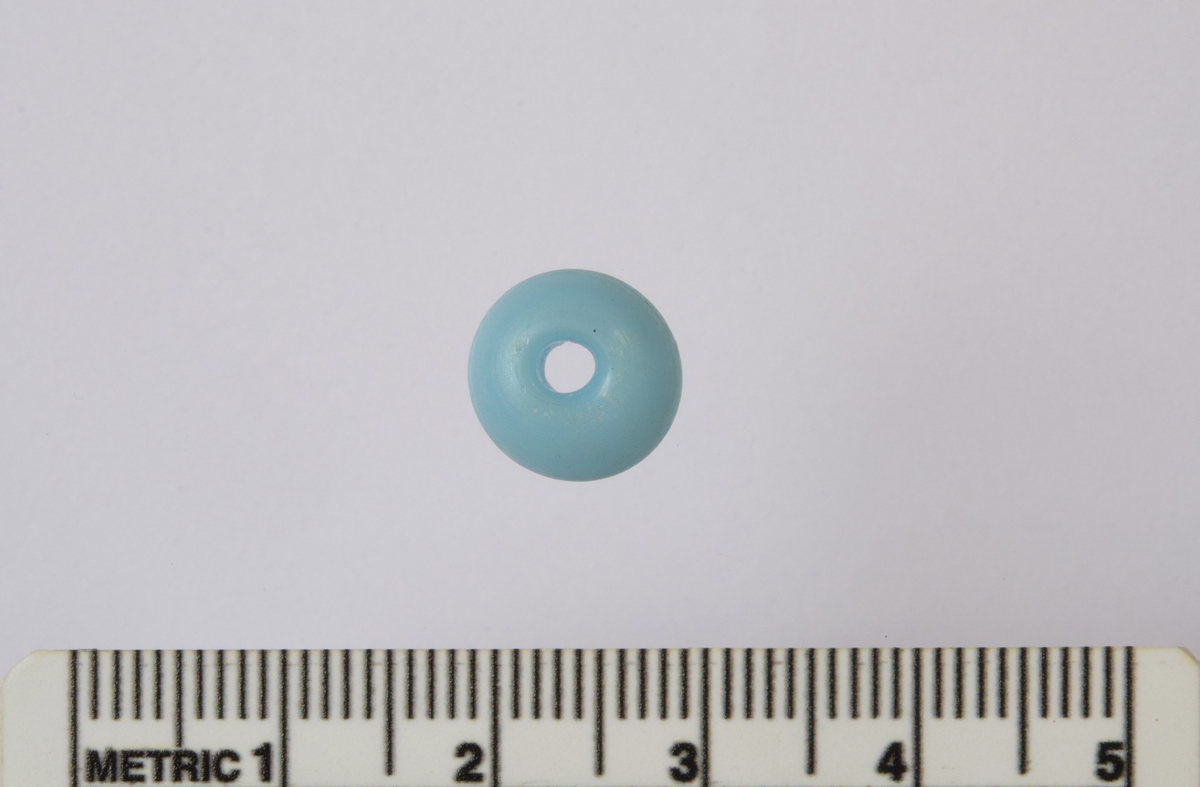 En opak lys blå glassperle. Med et hul i midten til monteirng på snor. Gjenstanden har en ytterst velbevart original overflate uten skader eller deformiteter. Alder er uavklart. Perlen har en samlet vekt på 0,9 g, en diameter på 1,0 cm, en høyde på 0,65 cm og hullet i midten har en diameter på 0,2 cm.
Fnr. 202030