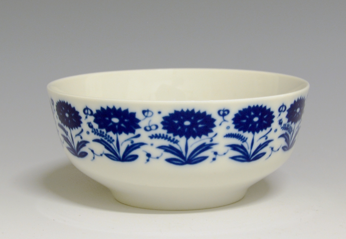 Sausebolle med fat, av porselen. Dekorert med blomsterdekor i blå iglasur trykkdekor.
Modell: Meny, 2310 av Tias Eckhoff, i produksjon fra 1955.
Dekor: Nellik av Anne-Marie Ødegaard fra 1957.