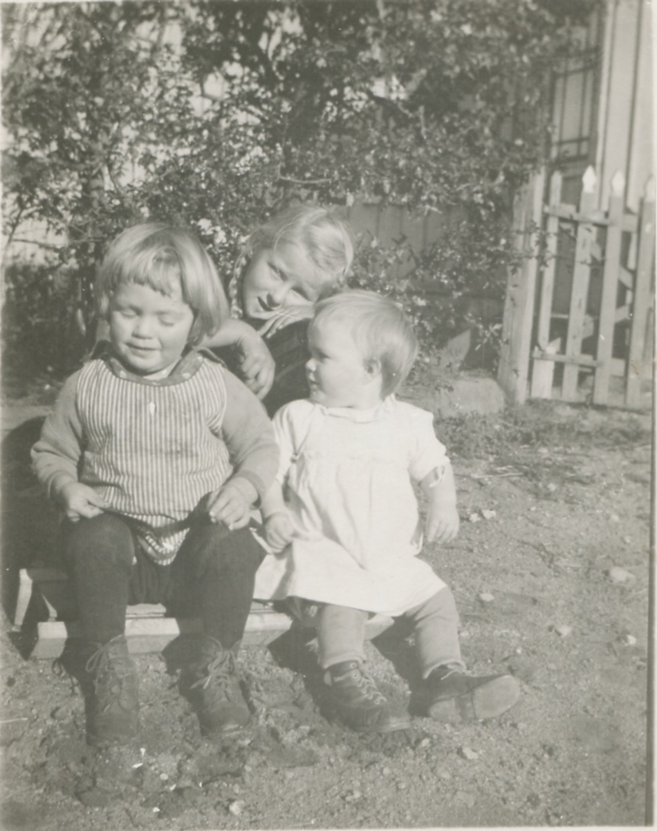 Tre barn sitter utomhus, Backen eller Högen (nedre gården) cirka 1926 - 1927. Från vänster, längst fram, ses Karl Gustav Pettersson (1924 - 2009) och brodern Gunnar Pettersson (1925 - 2016). Bakom dem sitter Birgit Pettersson (född 1920 eller 1921).