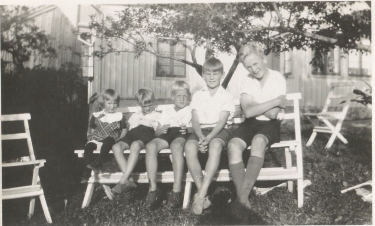 Fem barn sitter på en bänk i trädgården utanför Backen eller Högen (nedre gården), okänt årtal. Från vänster: 1. Okänd flicka. 2. Per Olof Bergendahl, sommargäst. 3. Bengt Bergendahl, sommargäst. 4. Åke Bergendahl (1925 - 1985), sommargäst. 5. Gunnar Pettersson (1925 - 2016), Högen.
