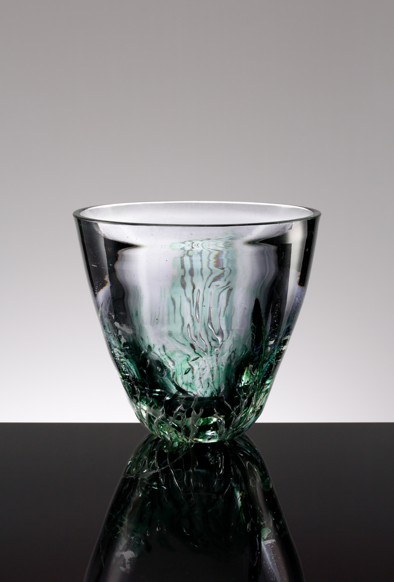Formgiven av Edvin Öhrström. Arielvas. Ljusgrå med omvänt konande form. Dekor i vasens nedre del, grönt sjögräs med ett abstrakt luftmönster.