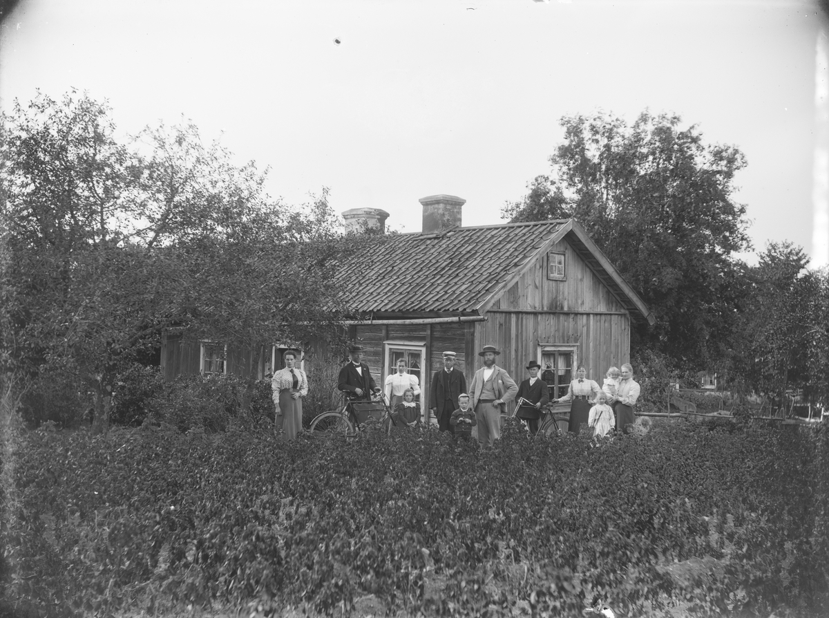 Bostadshus, släktgrupp 12 personer framför huset. 
Skräddare Ringström, Ormesta, Almby socken.