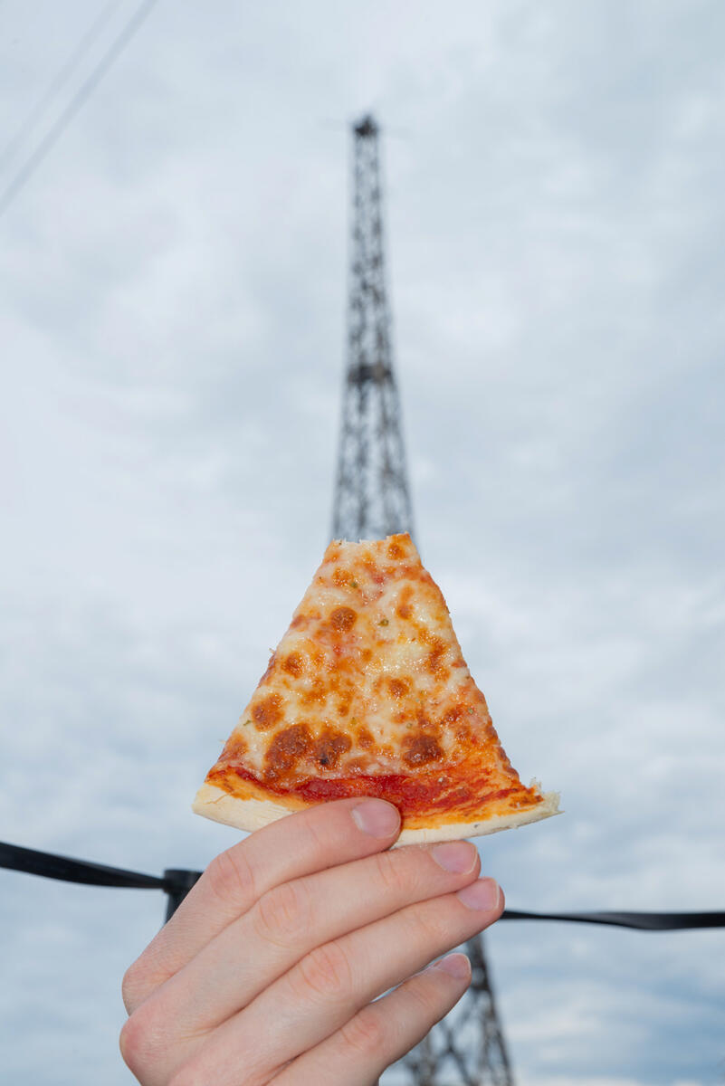 Bilde av Eifelltårnet med en hånd som holder et halvspist pizzastykke foran. Stykket danner basen på tårnet.