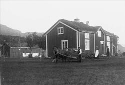 Folk med hest og høyvogn på gårdstunet foran et hus på Vikel