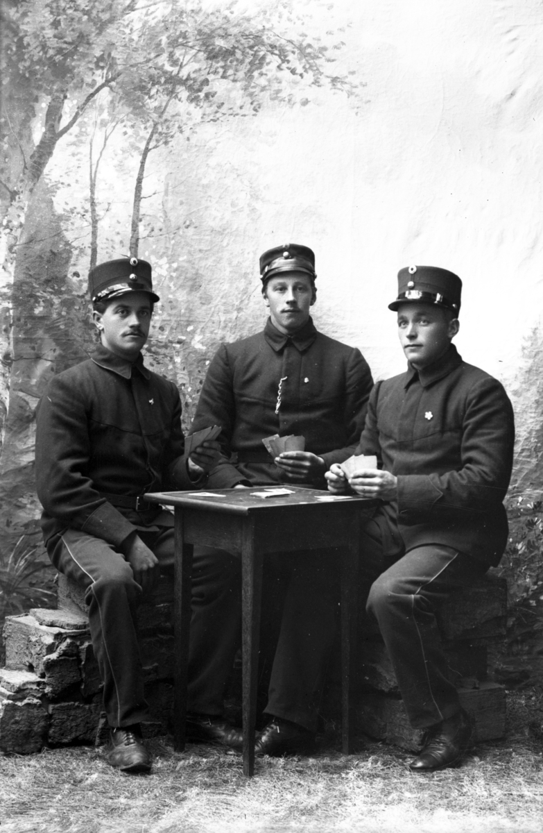 Atelierfoto.Tre soldater sitter ved bord og spiller kort.