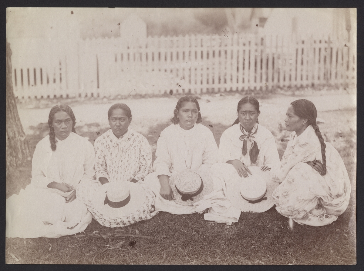 Bilden visar fem alvarlig blickande kvinnor som sitter på marken och håller halmhattar i handen.