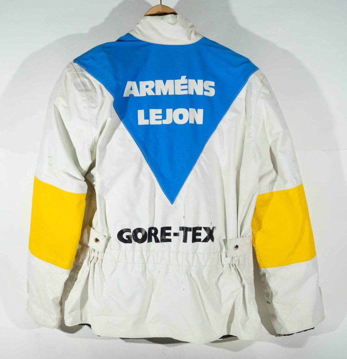 Vitt MC-ställ med jacka och byxor med blå och gula detaljer.  På vänster sida av bröstet på jackan "Armén" och på ryggen "Arméns Lejon" och "Gore-Tex".