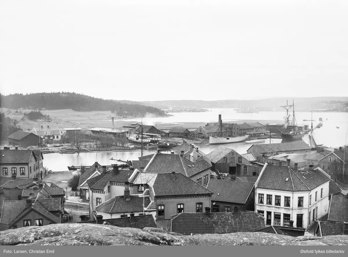 Sannesund i Sarpsborg med seilskuter på Glomma. Tomaster og en master.
Forretning til O. Eger i forgrunnen til høyre.
