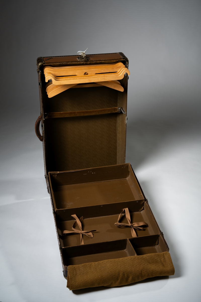 Koffert, resegarderob av märket Hartmann, av brun kartongpapp med metallbeslag och nitade förstärkningar runt kanterna. Kofferten består av två delar med ett uppfällbart lock upptill på en kortsida, invändigt klätt med gul-brun sammet. Den nedfällbara delen innehåller fyra fack med bruna knytband av bomull, och mönstervävt gul-brunt tygöverdrag. Den upprättstående delen, för hängande kläder, har sju galgar (tre modeller), varav en något skadad. Ett tvärgående band av sammet finns för att hålla kläderna på plats. Kofferten är låsbar. Handtag av läder finns på en kortsida och en långsida. Märke med flera patent sitter på en av kortsidornas insida.

På kofferten finns flera märken:
HARTMANN TOUROBE WARDROBE CASE Made in Racine, Wis., USA Reg. US. Pat. Office / Gibraltarized 
PAUL U. BERGSTRÖMS AB. STOCKHOLM
Nycklar och lås är präglade: 
YALE & TOWNE MFG.CO / MADE FOR HARTMANN H 40 I / MADE BY YALE