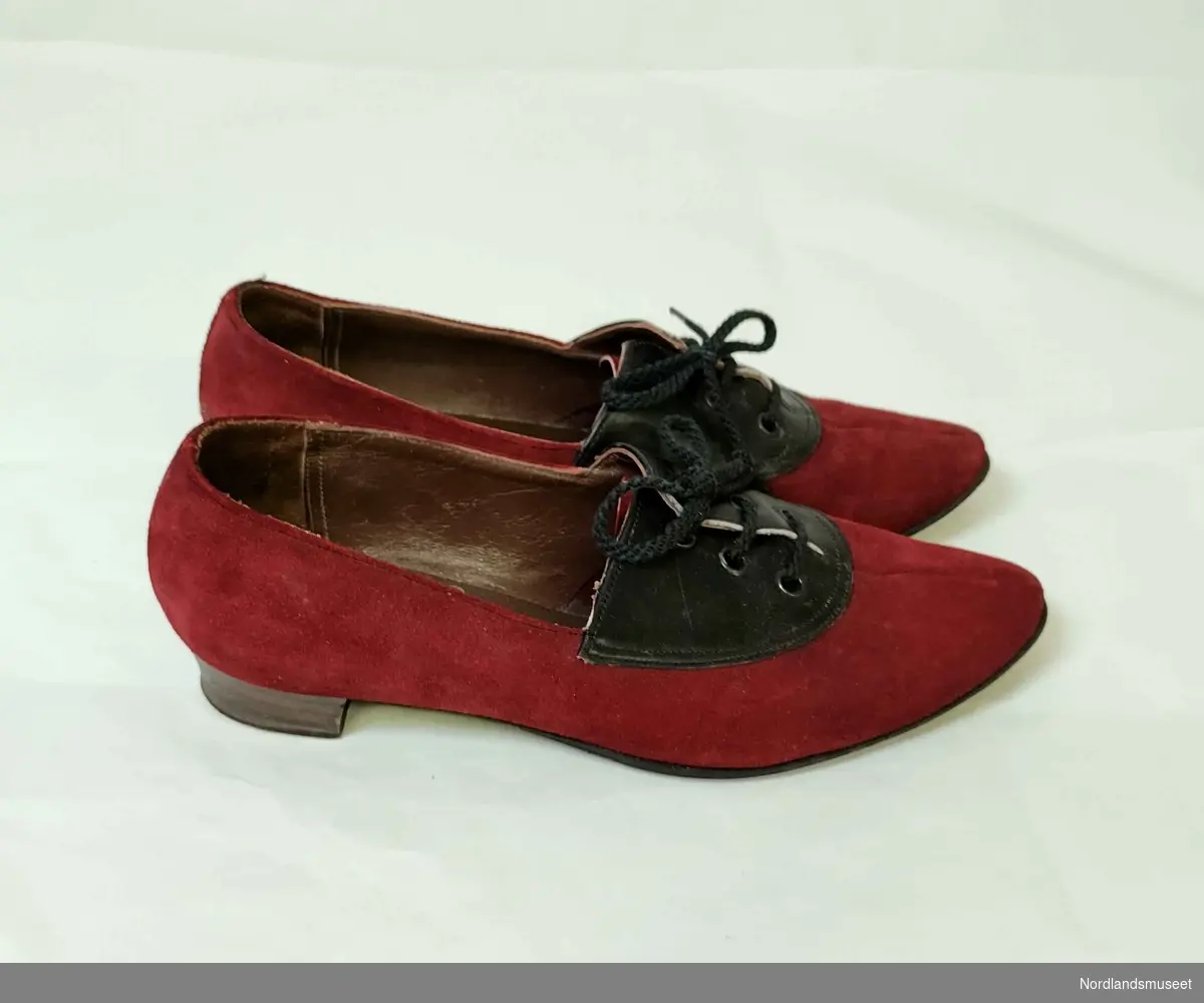 Snøresko til dame med hæl. Skoen er laget i rødt semsket skinn med et felt i svart skinn i front. I skoene er det lagt sydde såler som kan være hjemmeproduserte. Str. 5. Blå og hvit original skoeske.