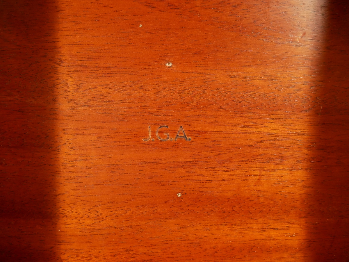 Fällbord av mahogny. Rund skiva med svarvat ben och tre fötter. Under bordsskivan är möbeln märkt J.G.A. = J.G. Axelssons snickeriverkstad.