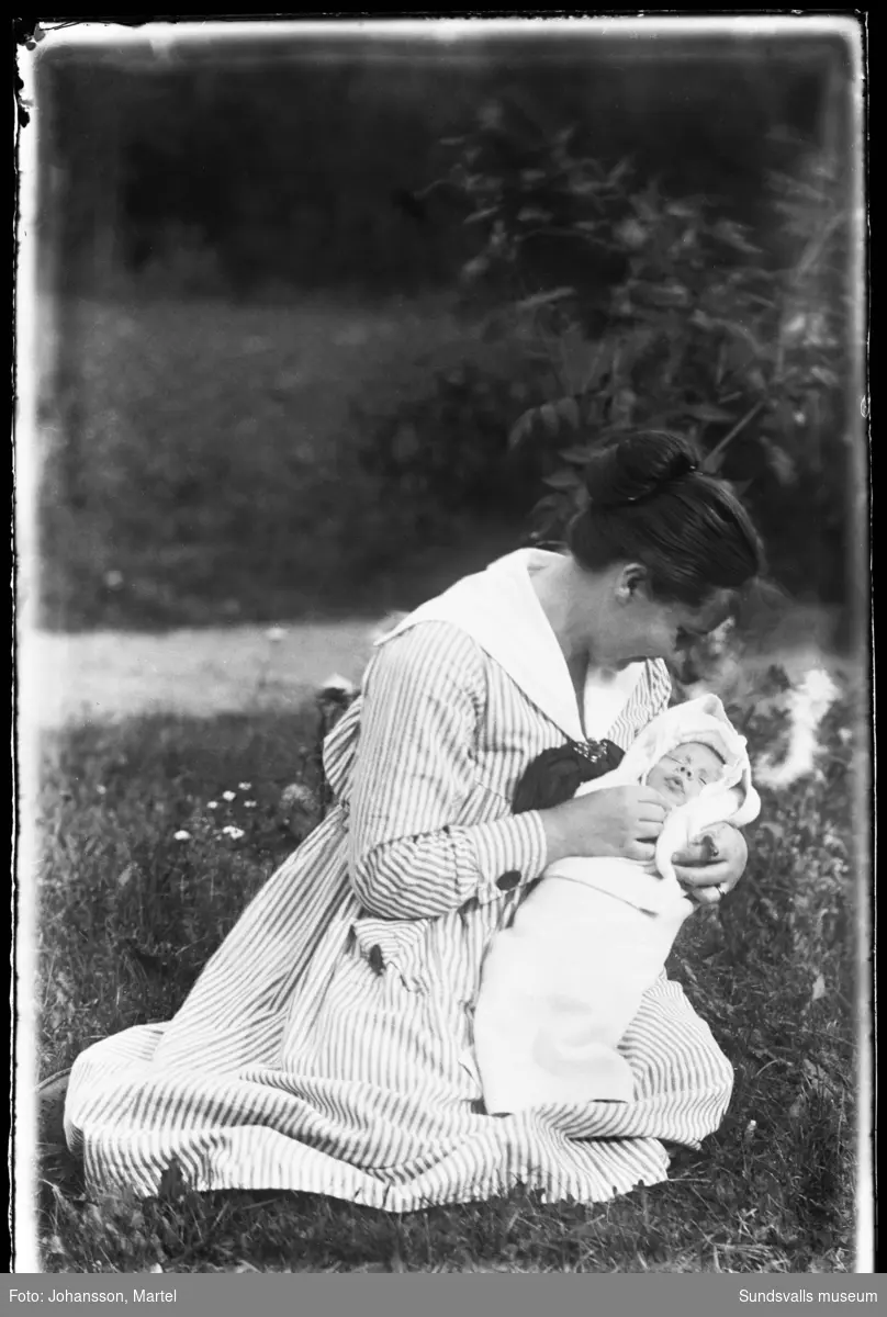 Porträttbild med en kvinna i gröngräset med ett spädbarn i famnen.