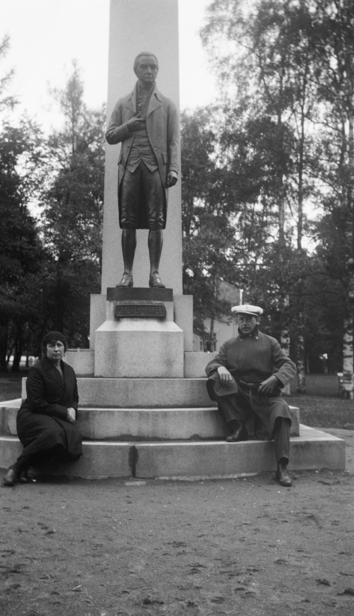 Maria og William sitter ved Carsten Anker monumentet ved Eidsvollbygningen på Eidsvoll