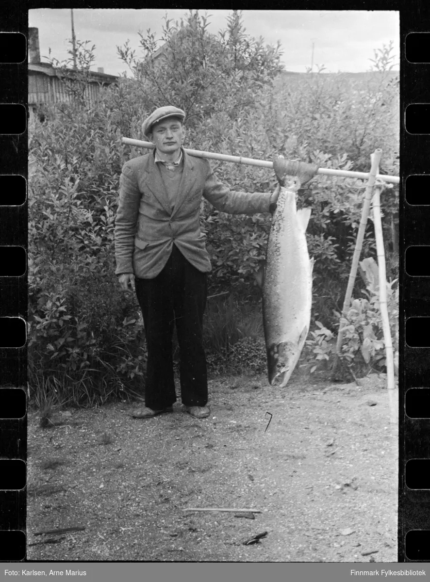 Mannen med laksen heter Helge Strømme fra Kirkenes. Sannsynligvis er laksen tatt i Pasvikelva på Elvenes. Mange i familien forteller at han var en ivrig laksefisker. Bildet er tatt utenfor hjemmet hans i Pasvikveien 14 i Kirkenes.

Foto antagelig tatt på slutten av 1940-tallet, tidlig 1950-tallet i Kirkenes