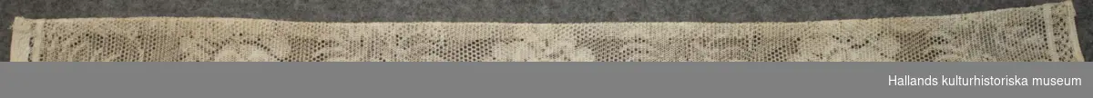 Två tillklippta gardinlängder samt tillhörande omtag av vit bomull (vävt) i spetsmönster. Längd 188 cm. Bredd 97 cm. 
Omtag: Längd 95 cm. Bredd 5,8 cm. 
Längderna är ofållade.