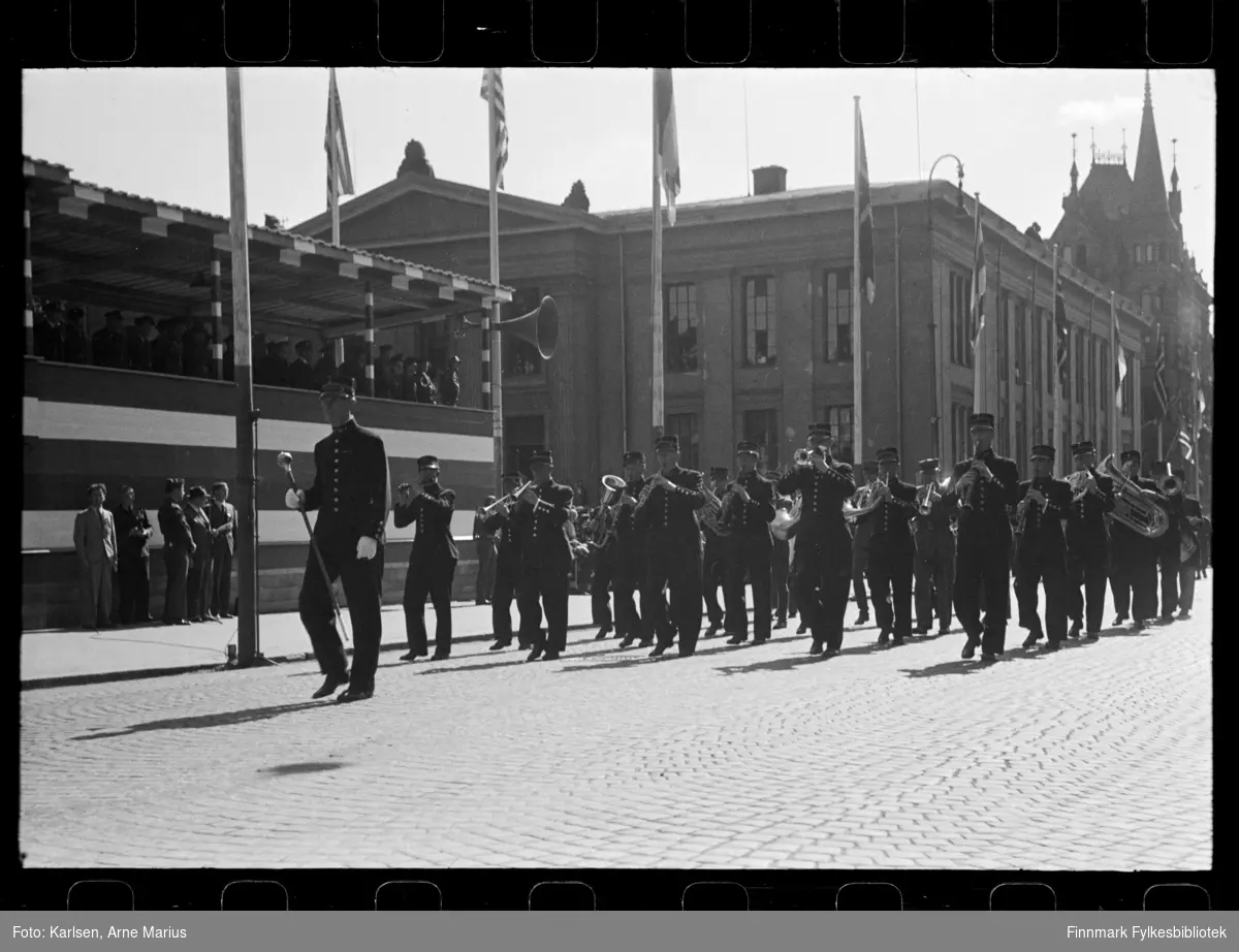 Et korps spiller musikk i det det paserer en tribune med offiserer. Tribunen var satt opp foran Universitetsplassen på Karl Johan 

De er en del av paraden på de alliertes dag den 30. juni 1945 (The Allied Forces day) i Oslo. 
