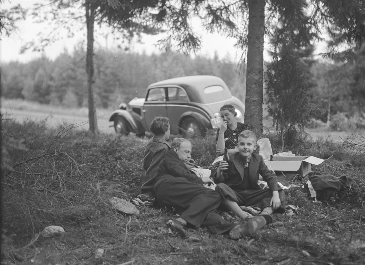 Picknick, fyra personer i gräset. En bil. 
Ture Källen, Märta, Jan Jerker Källen.