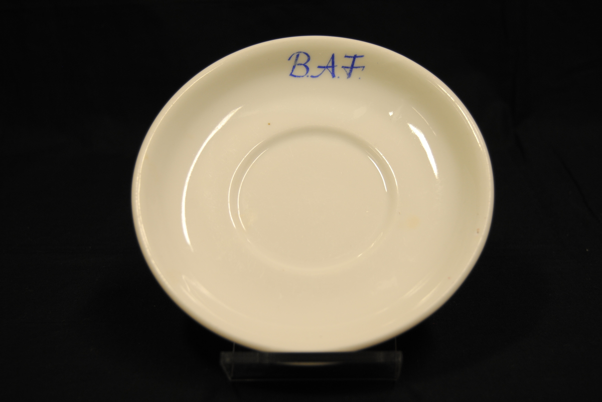 Rund kaffeskål av hvitt porselen med påskrift i blått: "B.A.F".
