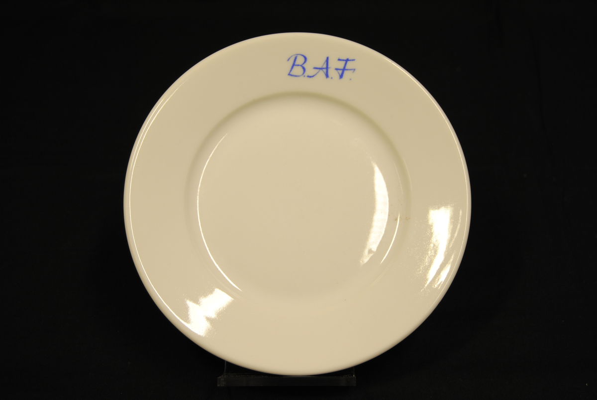 Rund asjett av hvitt porselen med påskrift i blått: "B.A.F".
