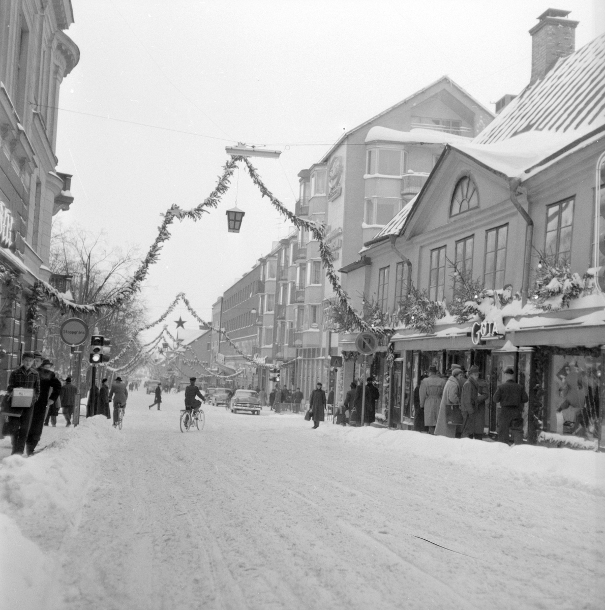 Julhandel i Linköping en snörik dag vid 1950-talets senare hälft. Storgatan är stämningsfullt juldekorerad och i hörnet mot Sankt Larsgatan råder trängsel till varuhuset Göta. Trafikljusen i vägkorset hör till stadens första, från 1952 och därefter.
