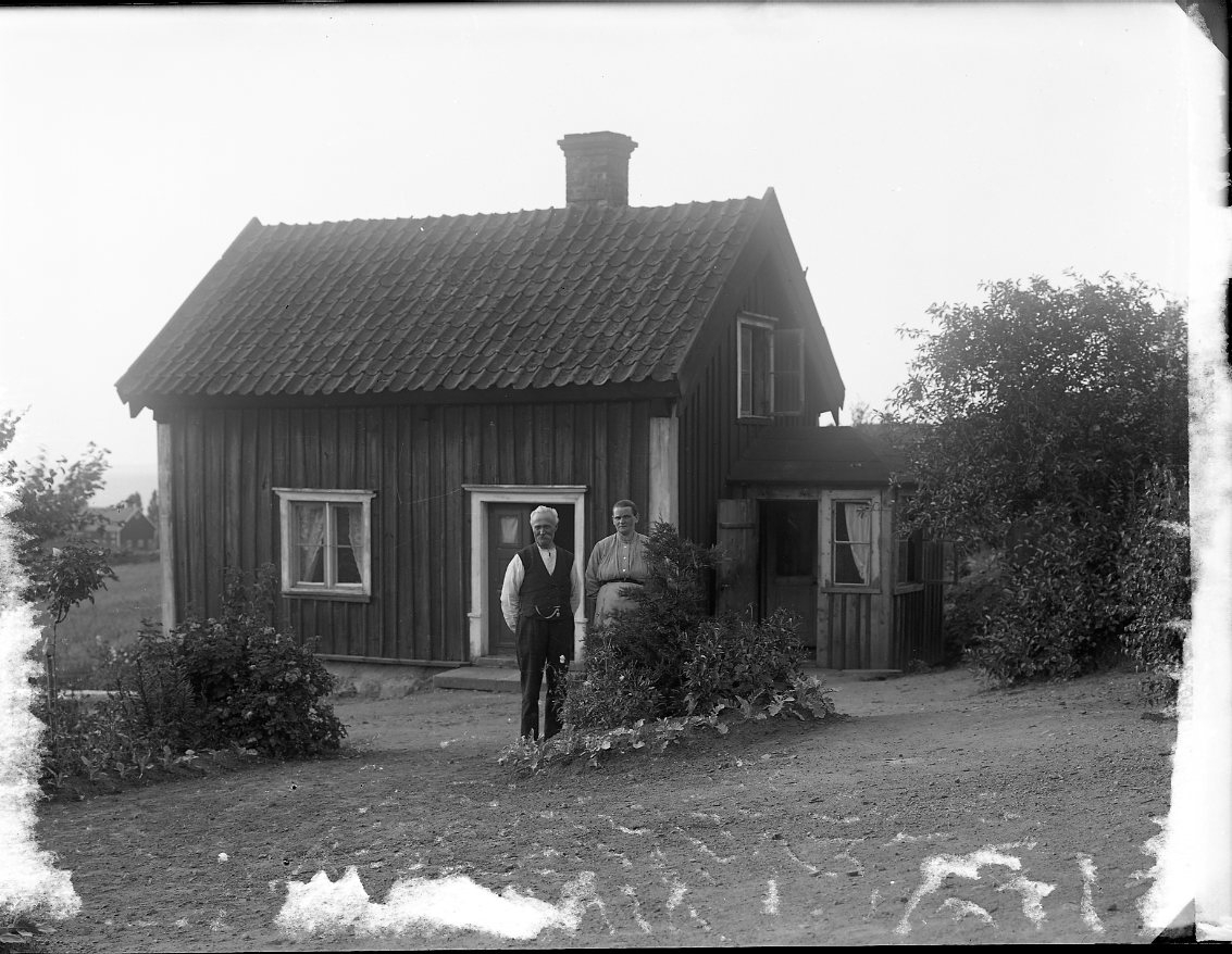 En man och en kvinna på en gårdsplan framför en liten stuga.