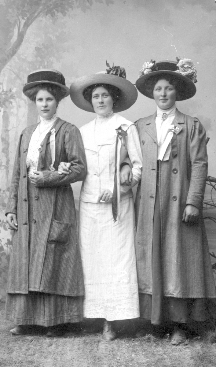 Tre kvinner med hatter, kjoler og 17. maisløyfer.
