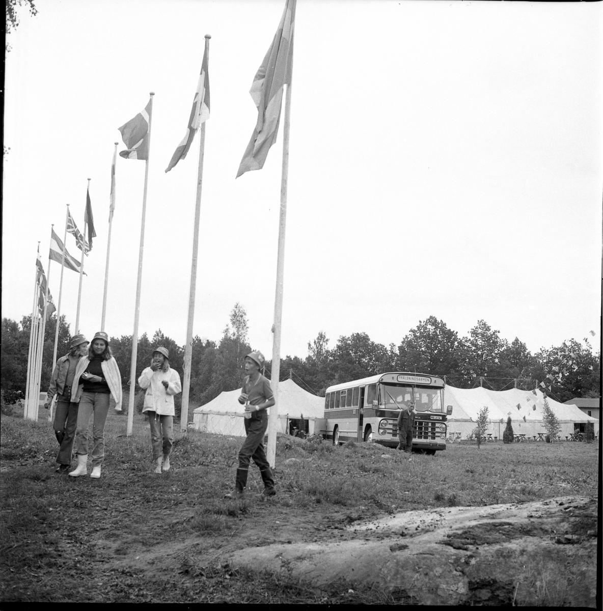 Ett fält med tolv flaggstänger och internationella flaggor, stora tält och en buss skyltad "Frälsningsarmén". En grupp ungdomar i förgrunden.