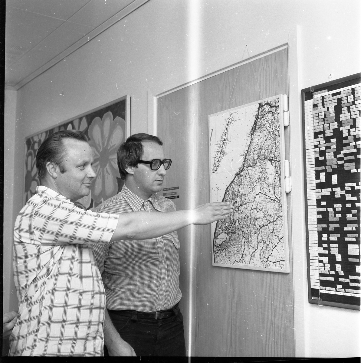 Två män står framför en karta som utvisar Vista härad, det är skolledning som diskuterar skolskjutsorganisation.