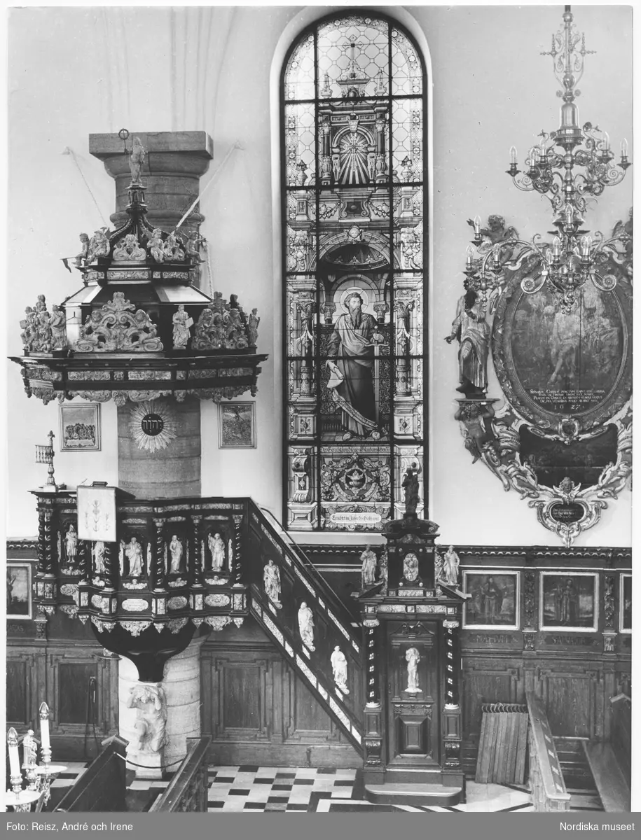 Stockholm. Interiör från Tyska kyrkan byggd 1642 av byggmästaren Hans Jakob Kristler från Strasbourg. Predikstolen är från 1660 av ebenholts och alabaster. En knäböjande änglafigur av sten bär upp korgen, ljudtaket har en kupolliknande form smyckad med skulpturer och ornament. Glasmålningarna uppsatta mellan 1878 och 1911  är tillverkade av firman F. Zettler i München.